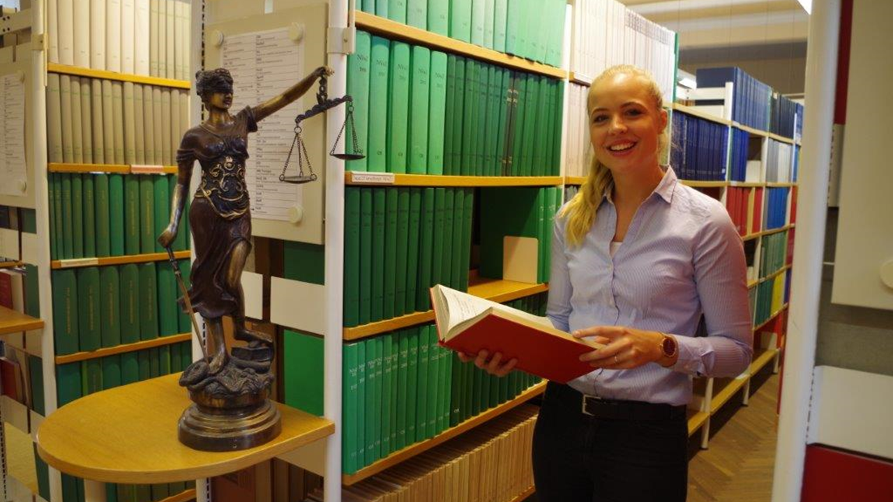 Bild: Eine Mitarbeiterin der Justiz steht vor Bücherregalen in der Bibliothek des Brandenburgischen Oberlandesgerichts.